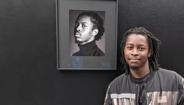 Young, Black young person with long braids stands in front of a portrait of themselves