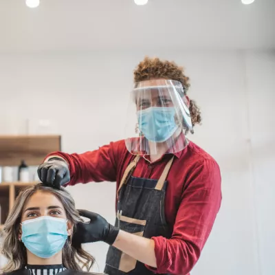 Young person wearing PPE, cuts a customer's hair