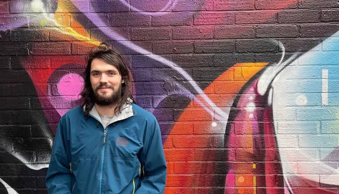 Young person with beard in front of graffiti wall