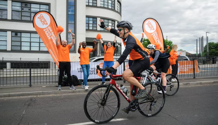 A Centrepoint cyclist cycling past a group of Centrepoint volunteers cheering