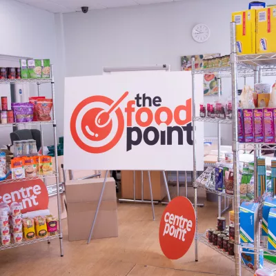 Photograph of The Food Point sign surrounded by metal shelves of food items such as sauces and cereals. The Centrepoint logo can also be seen.