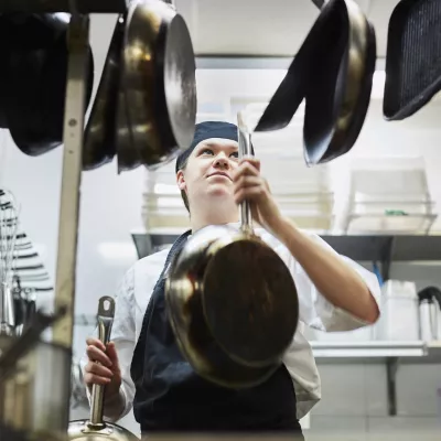 Young person in a professional kitchen hanging up pans