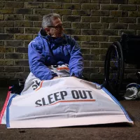 Man sits outside in a Sleep Out branded paper sleeping bag