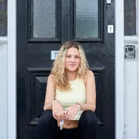 A young woman sits on the doorstep of her home, peacefully holding the keys