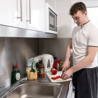 Young person stands chopping peppers in a kitchen