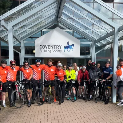 Staff at Coventry Building Society stand outside the office with their bikes, wearing orange Centrepoint cycling jerseys, ready for their sponsored bike ride