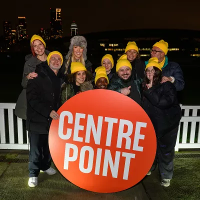 Selfridges staff stand in front of the Centrepoint logo, wearing yellow hats on the night of their Sleep Out fundraising event