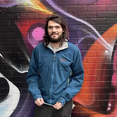 A young man leans against a wall, looking happy.