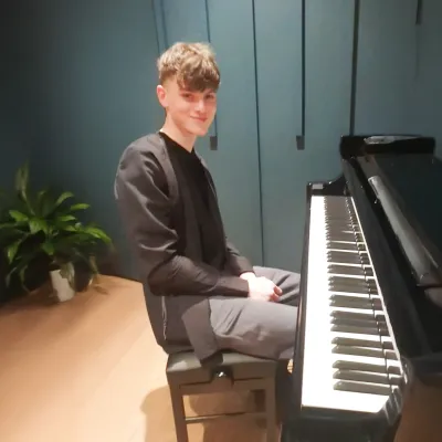 A young man sits at a piano, proudly.