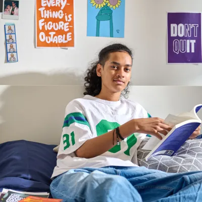Young person sitting on a bed, smiling, looking to camera.