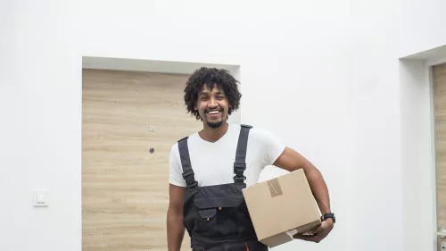 Person stands in front of door with a cardboard box tucked under one arm.