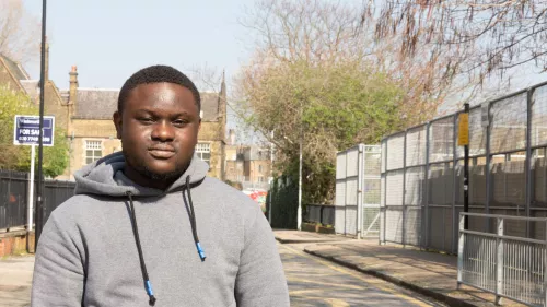 Young person stood outside on a road with fencing and road signs in the background.