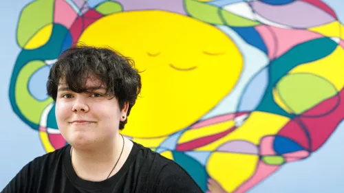 Photograph of young person against a brightly coloured mural.