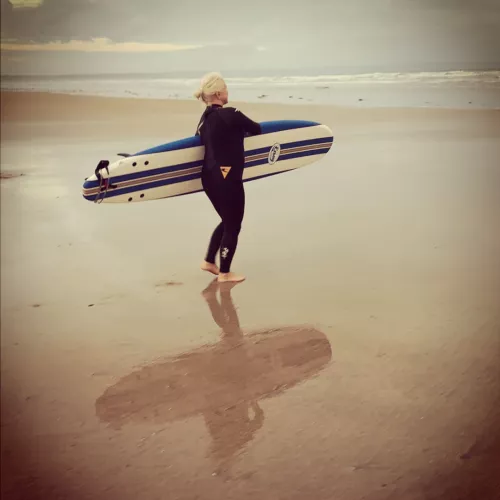 Person on empty sandy beach carrying surfboard to the sea