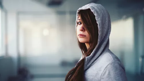 Homeless young person in a grey hoodie, looking to the camera upset.
