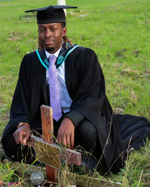 Young person in graduation outfit sitting by grave