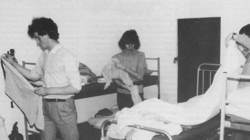 Black and white photograph showing three people making up bedding at a Centrepoint night shelter in the 1980s