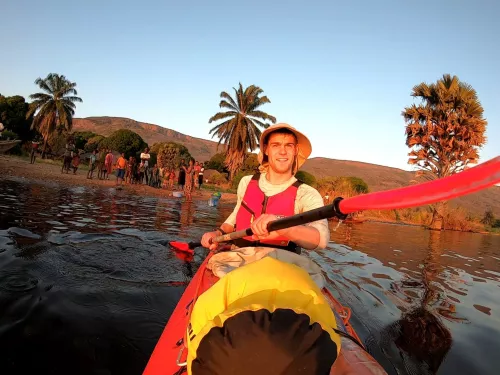 Photograph of Ben Harris, fundraiser, in a kayak on a lake. Ben is wearing a hat and trees can be seen in the background