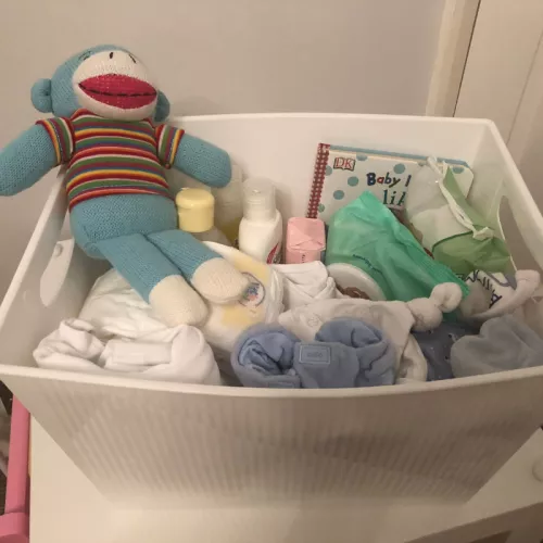 Photograph of a Centrepoint new baby box, with a blue monkey cuddly toy, toiletries, wet wipes and a children's book inside