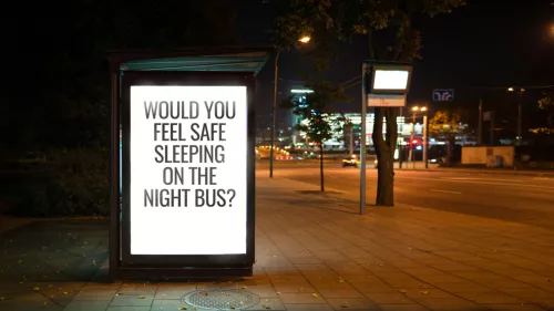 A photo of an advertisement hoarding on a bus stop at night, the advertisement asks one question: Would you feel safe sleeping on the night bus? 