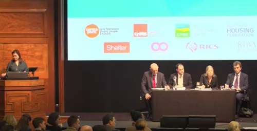 Video thumbnail of National Housing Hustings 2019 showing the host speaker at a podium and four speakers sat behind a table in front of a screen.
