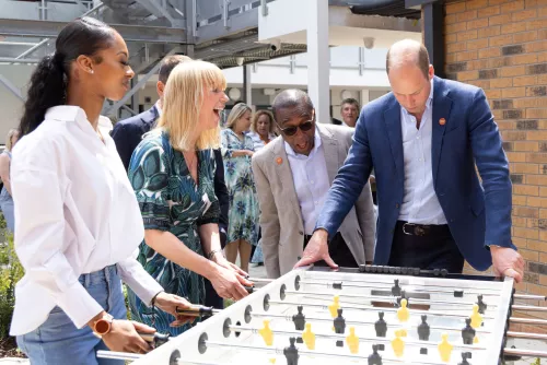 HRH Prince William and Sarah Cox playing table football with young people whilst CEO Seyi Obakin looks on.