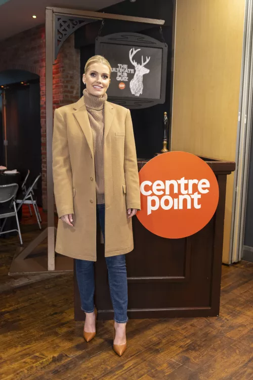 Lady Kitty Spencer smiles and stands in front of the Centrepoint logo in a pub.