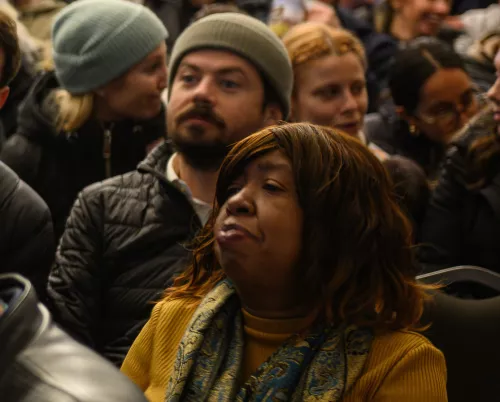 Black woman in foreground of an audience with other audience members behind her