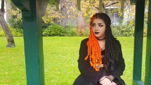 young person with orange and black hair extensions sitting at bus stop