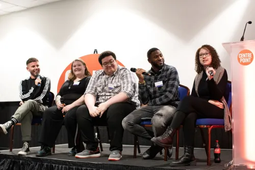 A group of speakers sit on the stage and cheerfully take part in a session