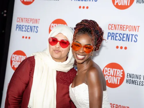 Two young people stand close together on the red carpet, wearing oversized glasses with orange lenses in front of a 'Centrepoint Presents' backdrop