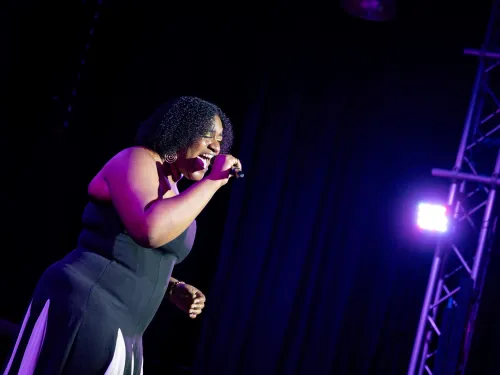 A young person wearing a black dress sings on stage 