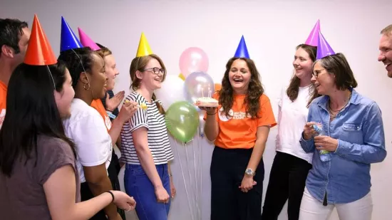 People wearing party hats, someone holding a cake