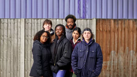 Group of 6 young people standing in front of a fence