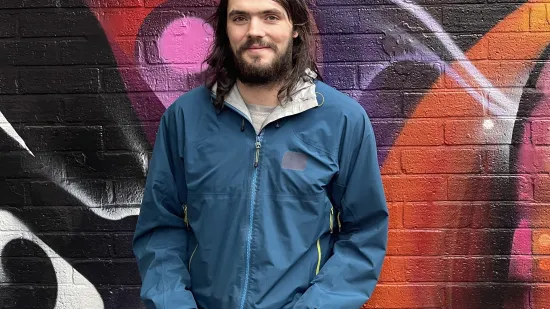 A young person stands in front of colourful street art looking hopeful