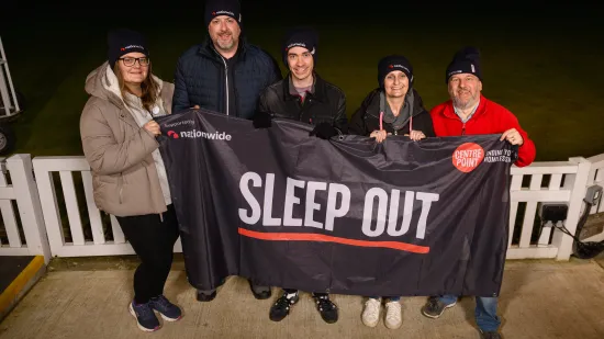 Partipants wrapped up in warm clothing hold up a banner during their Nationwide Sleep Out 
