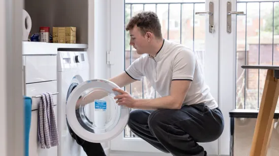 A young person puts laundry in the washing machine in their rented home