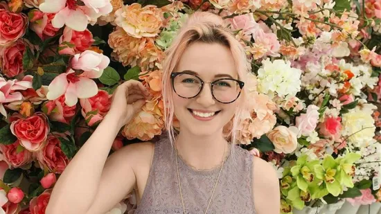 Young person with glasses standing in front of a flower wall