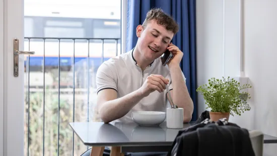 Young person on phone sitting stirring a cup of tea