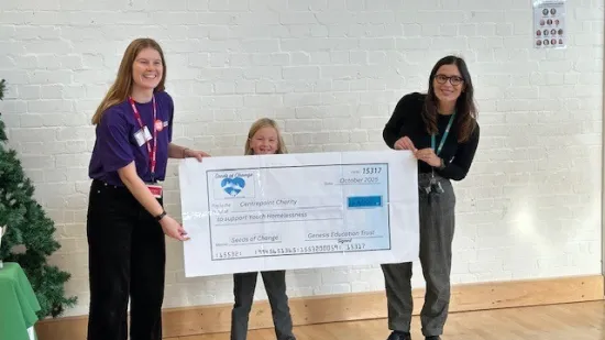Two women with lanyards and a child hold a large white cheque entitled to Centrepoint.