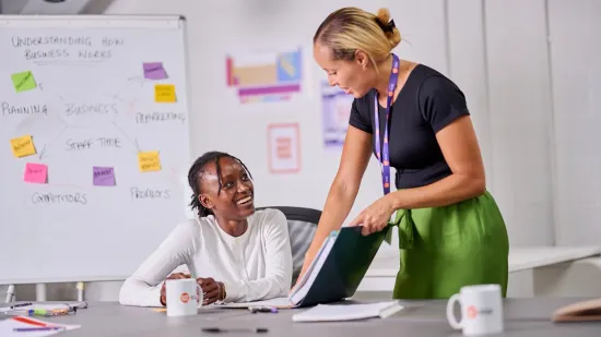 A Centrepoint team member shows a young person a book about managing finances in a classroom.