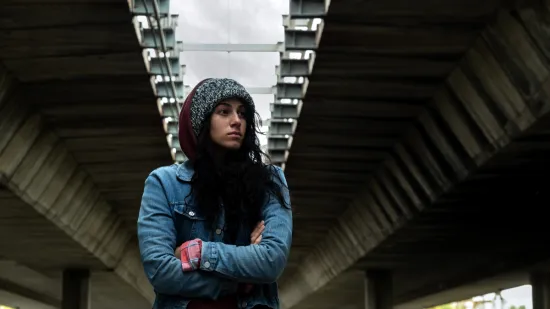 Young girl, bundled up in a jacket, gloves, and hat, arms crossed tightly against the cold, looking into the distance.