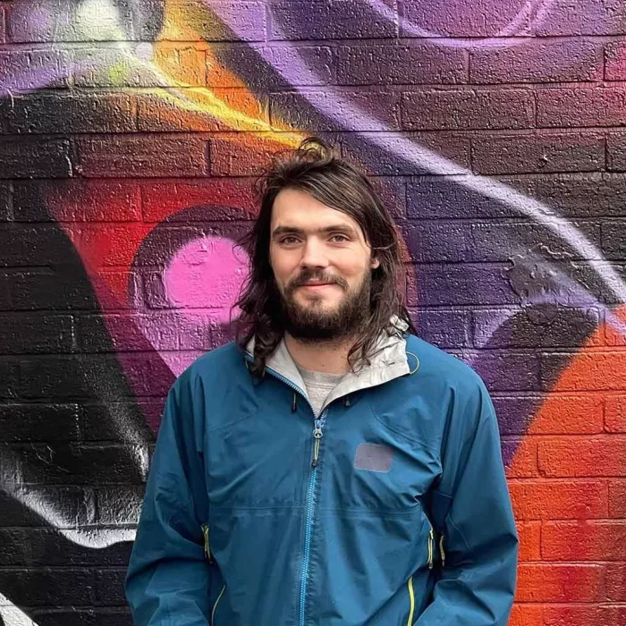 Young person with beard in front of graffiti wall