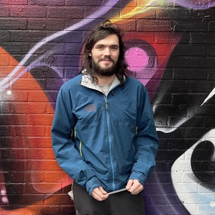 A young man leans against a wall, looking happy.