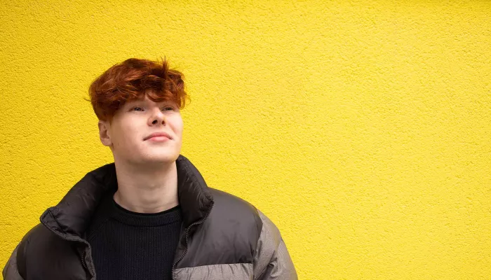 Young perons in front of yellow wall, looking up