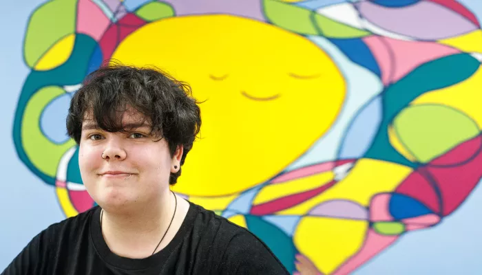 Photograph of young person against a brightly coloured mural.