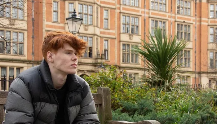 Young person sat outside on a bench looking off camera.