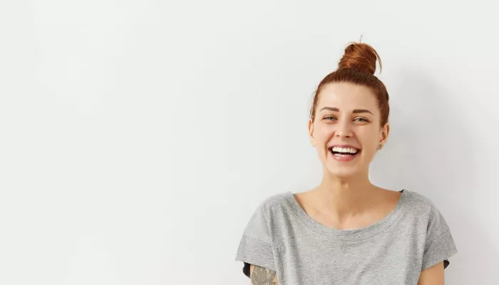 Young person stands against white wall whilst smiling at the camera