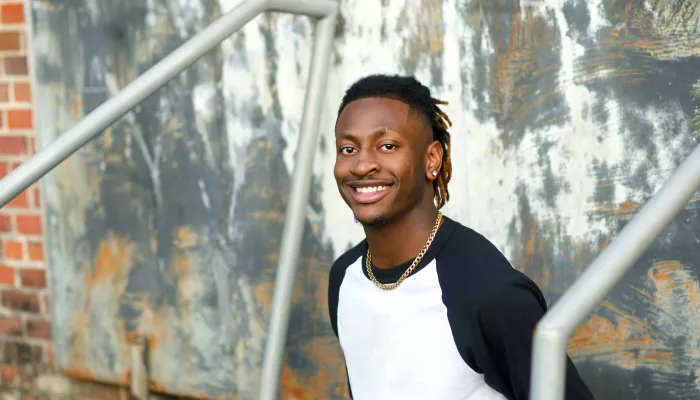 young black person with braids in a white and navy t-shirt in front of a wall