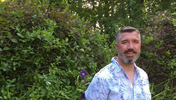 person in blue and white shirt standing in front of green foliage